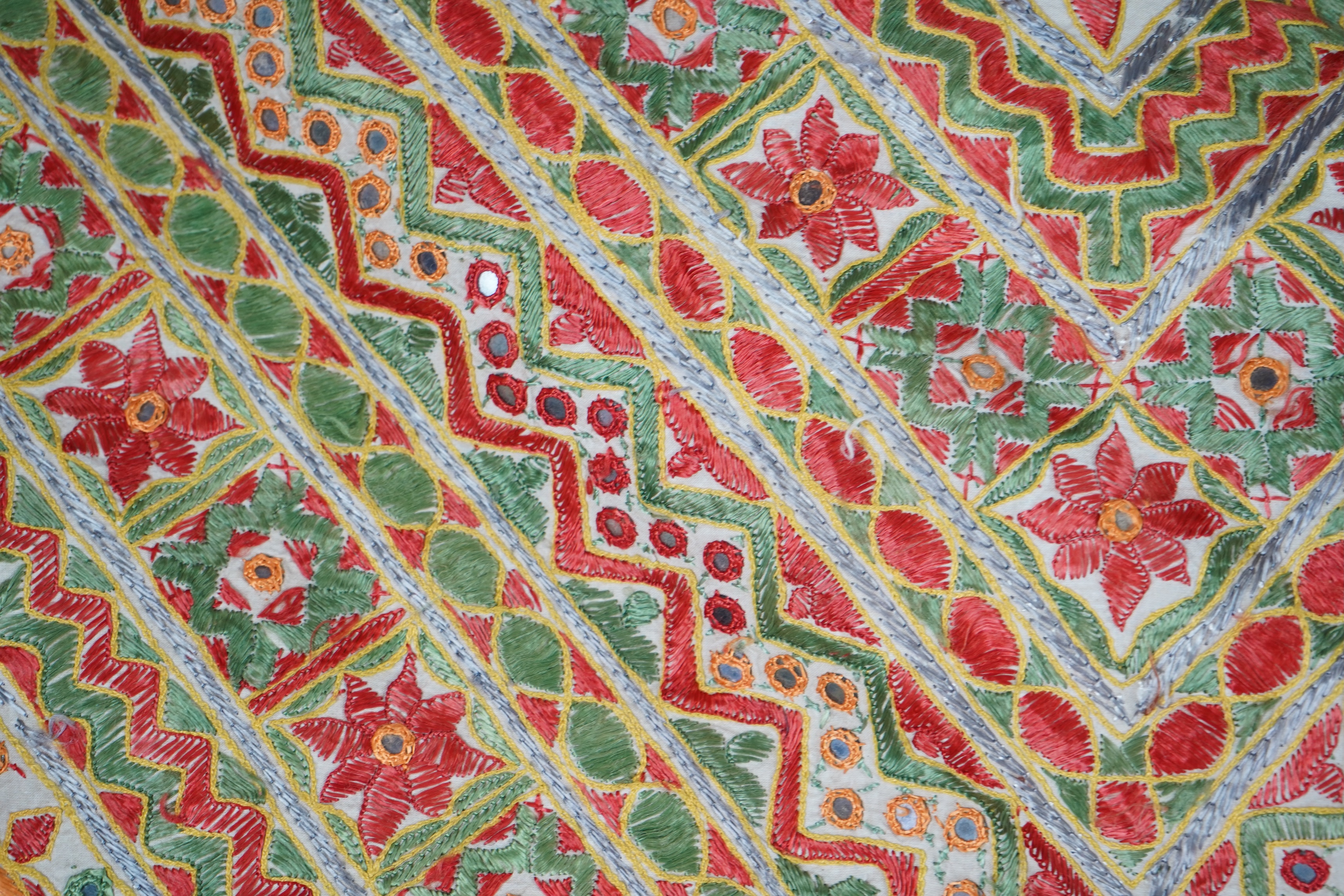 A large early 20th century Indian silk embroidered and mirrored wall hanging, heavily embroidered on a stone cotton ground, in green, orange, blue and ochre with small mirrored highlights throughout. 295cm x 250cm. Condi